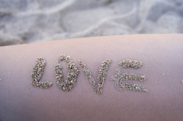 Kesätunnelma, Aurinkoinen ranta, rakkauden sanat hiekkaa iholla
. - Valokuva, kuva