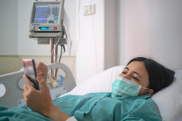 若い女性患者は病院のベッドに横にしてスマート フォン - 写真・画像