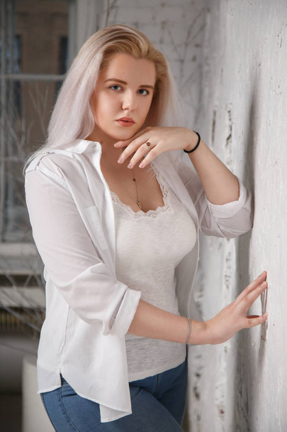 Portrait of a pretty big blonde in a white shirt on a gray background. - Foto, afbeelding