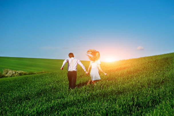Jonge gelukkige geliefden wordt uitgevoerd op de weide met groen gras en een blauwe hemel, aan de achterkant. - Foto, afbeelding