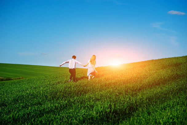Młodych kochanków szczęśliwy uruchomiona na łące z zieloną trawą i błękitne niebo, z tyłu. - Zdjęcie, obraz