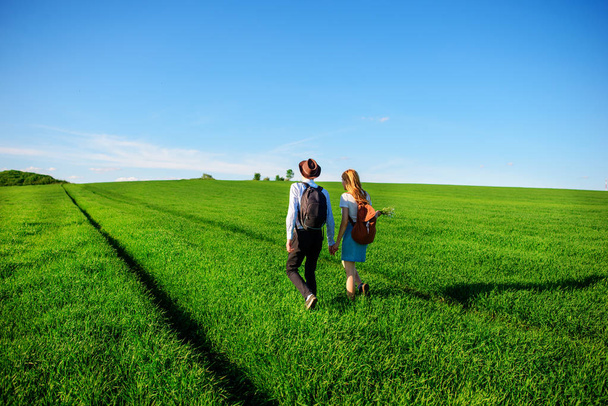 Con una mochila, un hombre con sombrero y una mujer con el pelo largo van por el camino. Una pareja camina por el prado
. - Foto, Imagen