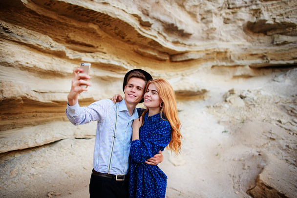 Viehättävä mies, jolla on kaunis nainen, halailee ja hymyilee. He tekevät selfietä hiekkalouhoksen taustalla.
. - Valokuva, kuva