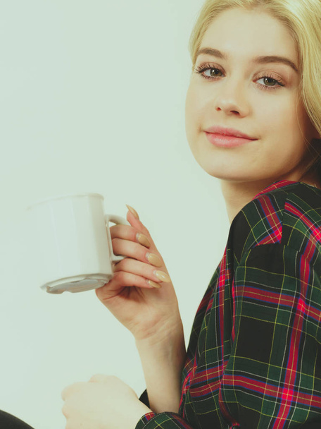 Pretty hipster young adult teenage woman sitting on sofa enjoying her leisure time drinking coffee or tea from mug. - Foto, Imagen