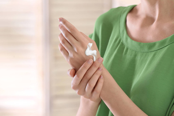 Young woman applying cream on her hands indoors, closeup - Foto, Imagen