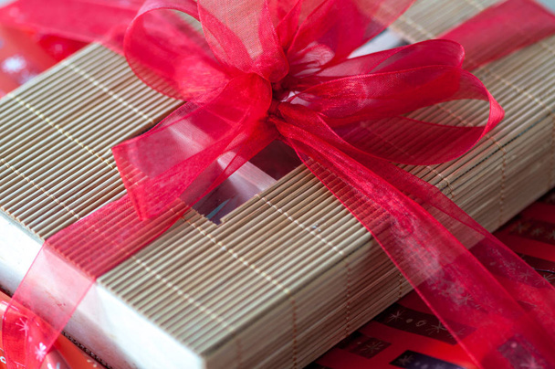 Крупный план подарка из красного банта, обернутого вокруг коробки из бамбуковых палочек
 - Фото, изображение