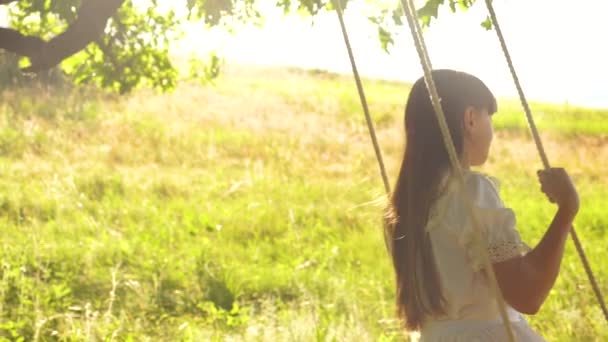schöne Mädchen mit langen Haaren schwingen auf Schaukel in leuchtend goldenen Sonnenuntergang und lächeln. Zeitlupe - Filmmaterial, Video
