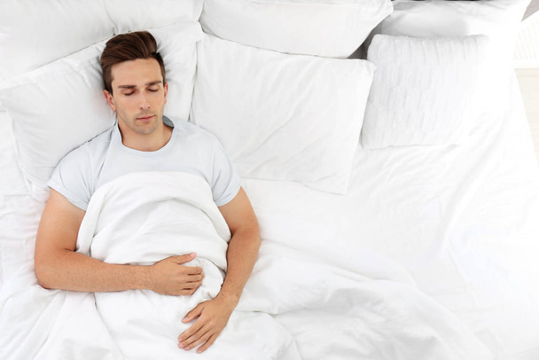 Young man sleeping on soft pillows in bed at home - Foto, afbeelding