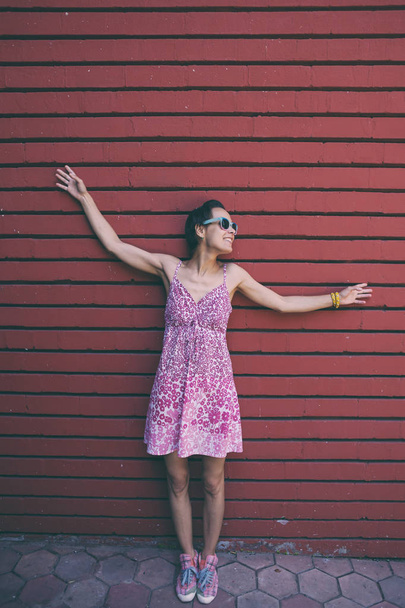 Chica en el fondo de una pared de colores. Una mujer con gafas camina por la ciudad. Morena delgada cerca de la pared roja
. - Foto, imagen