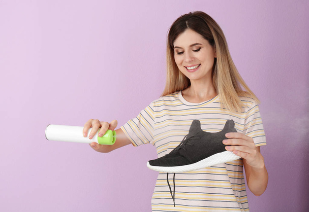 Woman spraying air freshener on shoe against color background - Foto, imagen