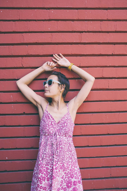 Meisje op de achtergrond van een gekleurde muur. Een vrouw in glazen is wandelen rond de stad. Slanke brunette in de buurt van de rode muur. - Foto, afbeelding