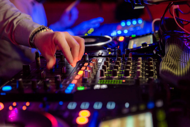 Professionele geluid mixer voor muzikale evenementen. handen van de Dj-operator in de lichte sfeer van kleurrijke achtergrond - Foto, afbeelding