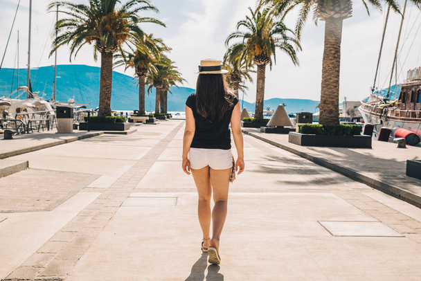 woman walk by sunny pier with palms. mountains and yachts on background - Photo, image