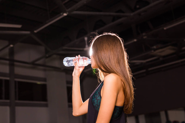 Fitness mujer joven bebiendo agua en el gimnasio. Mujer muscular tomando un descanso después del ejercicio
 - Foto, imagen