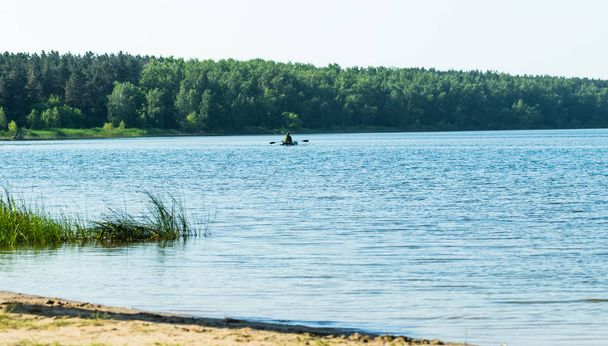 fisherman on a rubber boat on a lake, summer landscape - Zdjęcie, obraz