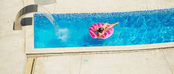 Enfant heureux jouant dans l'eau bleue de la piscine sur une station tropicale à la mer. Concept vacances d'été. Jolie fille nageant dans l'eau de la piscine. Enfant avec équipement de natation - cercle de natation gonflable
 - Photo, image