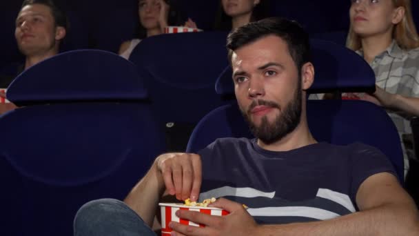 Atrakcyjne młody człowiek jedzenie popcorn podczas wytaczania filmu w kinie - Materiał filmowy, wideo