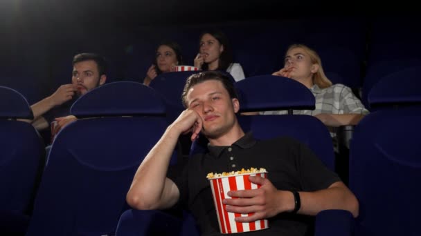 Young handsome man looking bored and tired sitting at the movie theatre. Attractive male spectator falling asleep at the cinema. Tired man watching movies. Entertainment, lifestyle concept. - Footage, Video