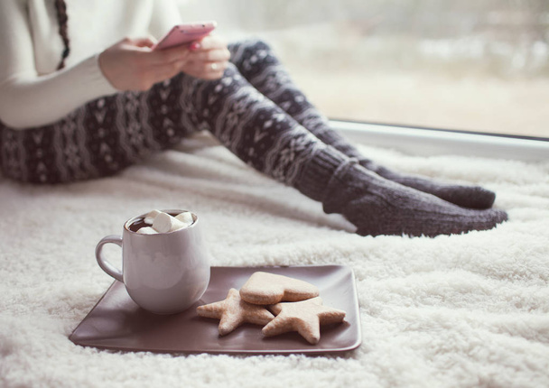Woman using smartphone and sitting near cup of cocoa with cookies - Photo, Image