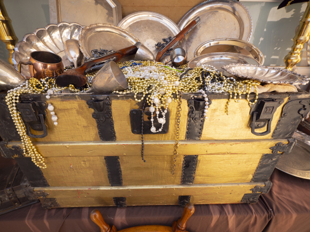A close up image of pirates chest treasures including, bead necklaces, guns and dinnerware. - Photo, Image