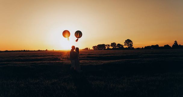 Pareja de amor de pie en el campo con bolas de helio de color
 - Foto, imagen
