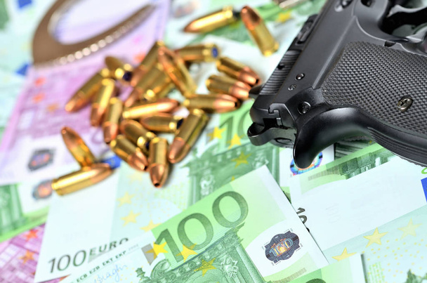 Σφαίρες, πιστόλι και χειροπέδες σε φόντο τραπεζογραμματίων ευρώ - Φωτογραφία, εικόνα