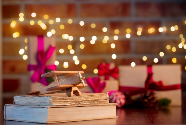 houten vliegtuig speelgoed en boeken op achtergrond met fairy verlichting en geschenken in de bokeh. Christmas Holiday seizoen - Foto, afbeelding