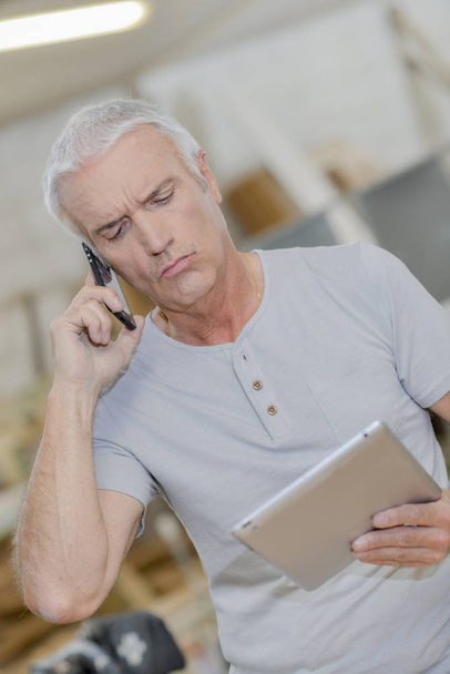 Man looking at tablet, on telephone, confused expression - Foto, Imagen