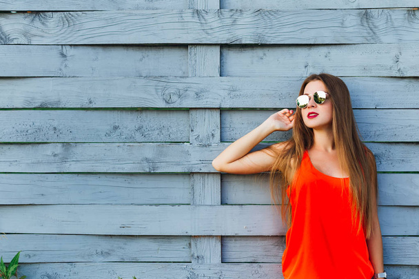 ragazza elegante in camicetta rossa e occhiali da sole appoggiati a una recinzione di legno
 - Foto, immagini