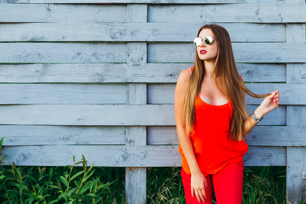 Az elegáns és modern lány, hosszú hajú, piros ruhát, a háttérben egy fából készült kerítés - Fotó, kép