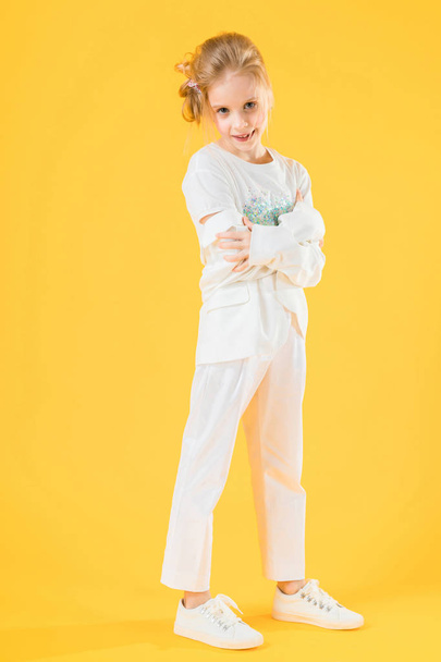 Una adolescente vestida de blanco posando sobre un fondo amarillo. La chica bajó su chaqueta hasta los codos. - Foto, Imagen