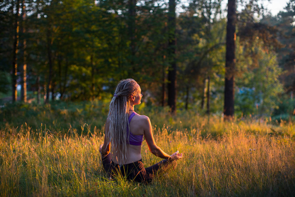Жінка йога з довгим волоссям дредлоки медитує на природі
. - Фото, зображення