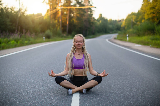 Mujer yoga medita sentada en medio del camino del campo
.  - Foto, imagen