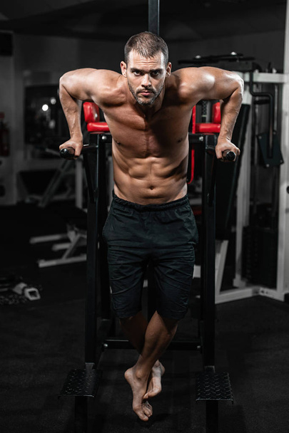 Muscular man doing push-ups on uneven bars in crossfit gym. Workout lifestyle concept - Photo, Image