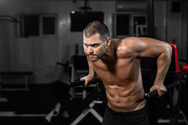 Muscular man doing push-ups on uneven bars in crossfit gym. Workout lifestyle concept - Fotó, kép
