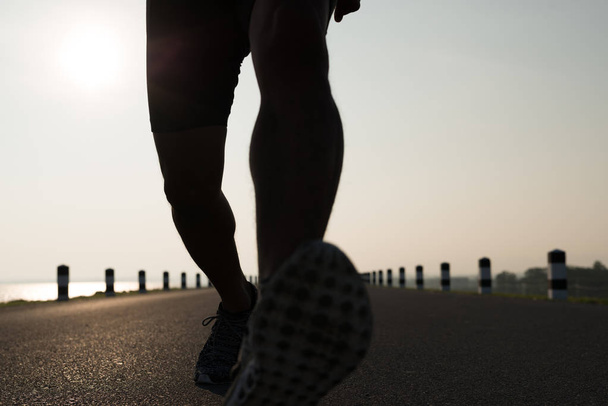 Blick nach unten auf einen Mann asiatische Beine, die in der Zeit während des Sonnenaufgangs auf Damm Straße Übung. Gesunder Lebensstil - Foto, Bild