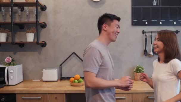 Beautiful happy asian couple are dancing in the kitchen at home. Young asian couple have romantic time while listening music at home. - Кадры, видео