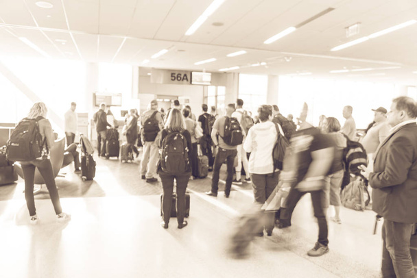 Vintage tone blurred diverse group of passengers with luggage waiting in line at airport boarding gate in USA. Blurry group of travelers queuing to onboard to jet bridge airplane, final boarding gate - Photo, Image
