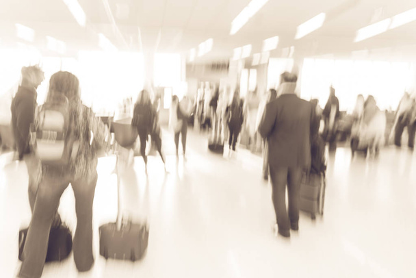 Винтажный тон размыл разнообразную группу пассажиров с багажом, ожидающим в очереди на посадку в аэропорту США. Размытая группа путешественников, стоящих в очереди на борт реактивного самолета-моста, посадка на посадку
 - Фото, изображение