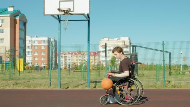 Vammainen mies pelaa koripalloa pyörätuolistaan, ulkona
 - Materiaali, video