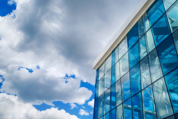 Onderaanzicht van moderne glas blauw business centrum architectuur, vrije ruimte. De reflectie van het zonlicht op abstracte gebouw van glas. Hemel met wolken achtergrond. Venstermodus hoek van kantoorgebouw - Foto, afbeelding