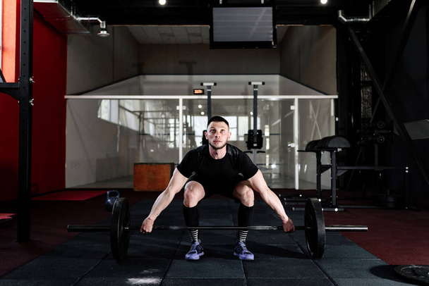 Fit young bearded athlete lifting the barbell in gym. Gym training. Full body length portrait - 写真・画像