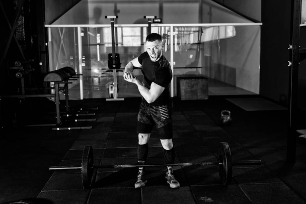 Screaming young man dressed in black t-shirt showing his biceps in gym. Man posing in gym and looking at camera while showing his biceps - Photo, Image