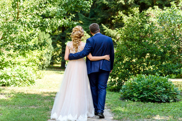 Happy bride and groom hugging and walking in park on wedding day. Wedding couple in love, newlyweds, free space. Bride and groom embracing in nature  - Fotoğraf, Görsel