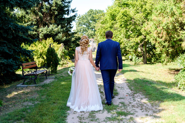 Happy bride and groom holding hands and walking in park on wedding day. Wedding couple in love, newlyweds, free space - Photo, image