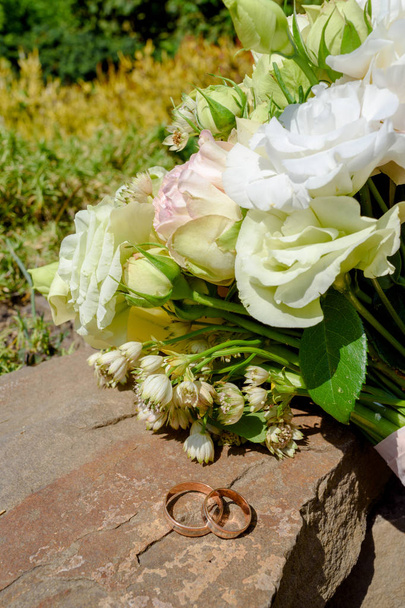 Two golden wedding rings on stone near   beautiful wedding bouquet of white and pink peony and roses in blur outdoors, selective focus, close up - 写真・画像