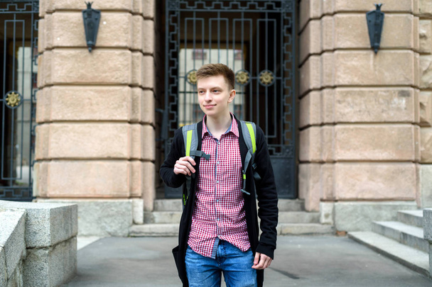 Portrait of stylish young man in plaid shirt and jacket with backpack walking in the city outdoors. Student travel, free space - Fotoğraf, Görsel