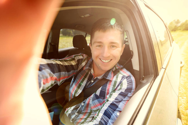 Wide angle selfie of happy young man from driver seat when road trip. Handsome young business man taking selfie using smart phone while sitting in car. Travel, transport, technology, people concept  - Фото, изображение