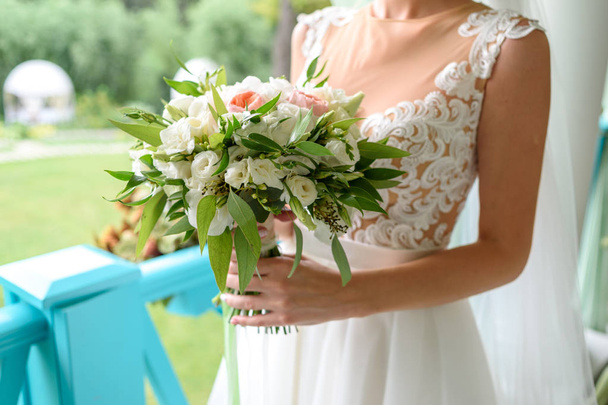Beautiful wedding bouquet of fresh white and pink roses and greenery in bride hands outdoors, free space. Bridal bouquet, close up - 写真・画像