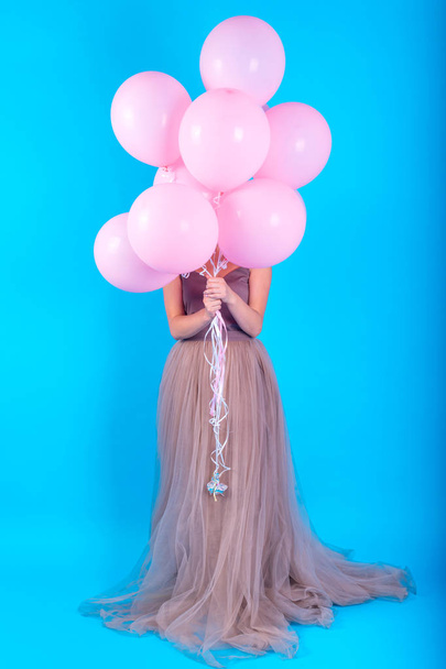 Beautiful young woman having fun with pink helium air balloons over blue background, full length body. Girl with curly hair in long dress holding balloons. Holidays, birthday, valentine concept  - Zdjęcie, obraz